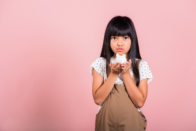 Małe azjatyckie dziecko w wieku 10 lat trzymające skarbonkę i patrzące w kamerę