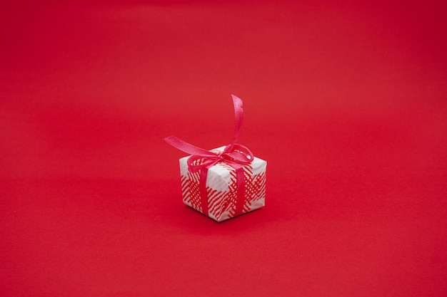 Małe biało różowe pudełko upominkowe z różową wstążką. Świąteczne pudełko na prezent. Na białym tle na czerwonym tle