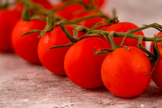 Małe czerwone dojrzałe pomidory na gałązce na brązowym tle