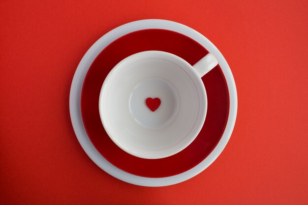 Małe czerwone serce na pustej białej filiżance na czerwonej powierzchni. Dieta minimalna koncepcja.