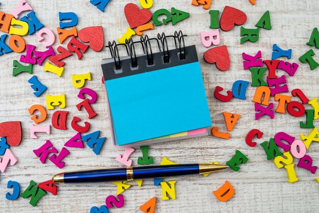 Małe drewniane losowe kolorowe litery z pustą notatką na stole do edukacji ABC