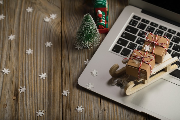 Małe drewniane sanie ze świątecznymi prezentami na laptopie Zbliżenie