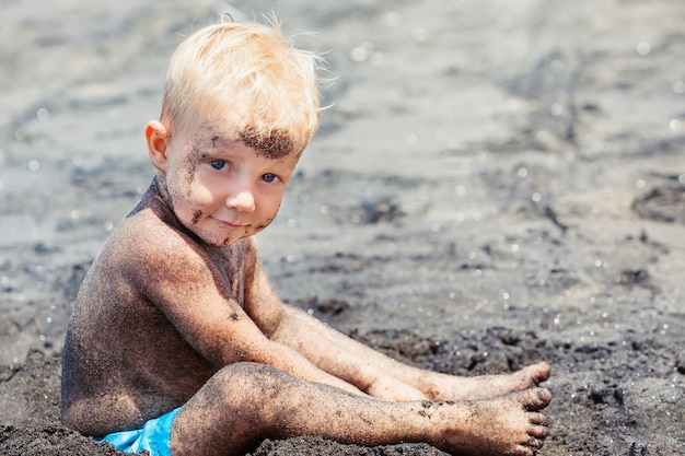 Zdjęcie małe dziecko bawi się czarnym piaskiem na tropikalnej plaży morskiej