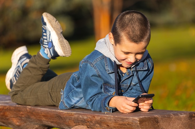 Małe Dziecko Chłopiec Grając W Gry Mobilne Na Smartfonie W Parku.