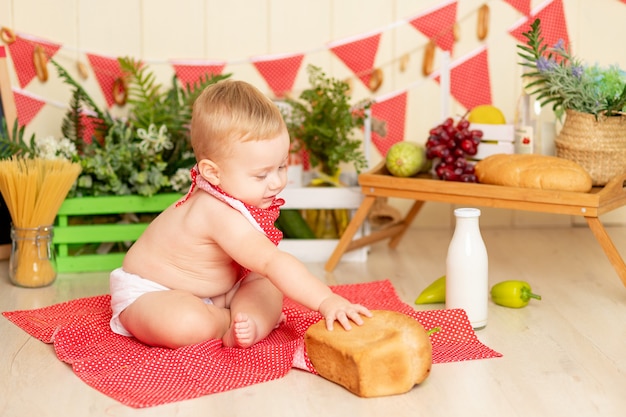 Małe dziecko, chłopiec, siedzi na podłodze w kuchni z bochenkiem chleba