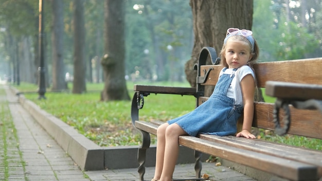 Małe dziecko dziewczynka siedzi samotnie na ławce w parku latem.