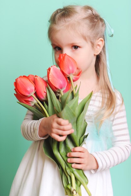 Małe dziecko dziewczynka trzymająca czerwone tulipany w stylowej sukience patrząc na kamerę