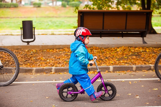 Małe dziecko jadące na rowerku biegowym, podążaj za rodzicami w jesiennym parku