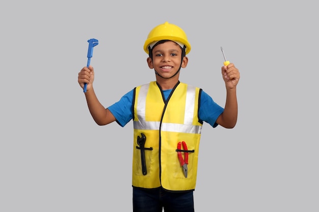 Małe dziecko jako pracownik na szarym tle Dziecko nosi hełm ochronny i trzyma w ręku narzędzia
