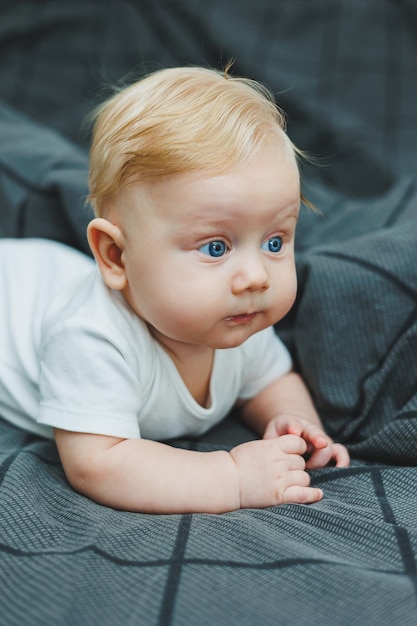 Małe dziecko leży na dużym łóżku w domu Portret pięciomiesięcznego dziecka leżącego na szarym łóżcu Wesołe szczęśliwe dziecko