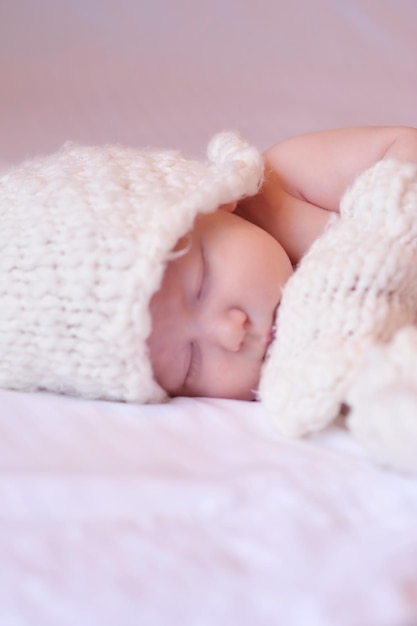 Małe dziecko niemowlę dziewczynka nosić czapkę z dzianiny leżąc w łóżku na białym zbliżenie. Dzieciństwo.