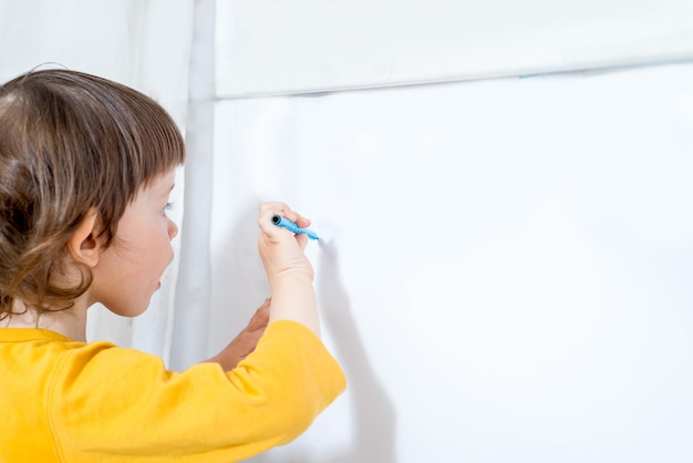 Małe dziecko rysuje flamastrem na białej tablicy Zajęcia domowe w izolacji