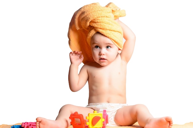 Małe dziecko siedzące obok zabawek na białym tle owinięte w żółty ręcznik