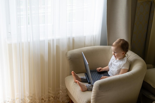 Małe dziecko siedzi na krześle i komunikuje się z tatą za pomocą komunikacji wideo przez laptopa