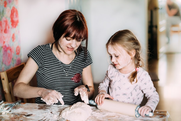 Małe Dziecko Stoi W Kuchni I Pomaga Mamie Przygotować Ciasto Z Mąki Całą Twarzą.
