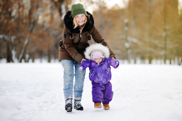 Małe dziecko uczy się chodzić. Młoda kobieta z dziewczyną za toddler w winter park