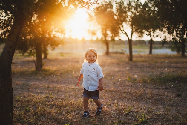małe dziecko uśmiecha się o zachodzie słońca w polu drzew oliwnych