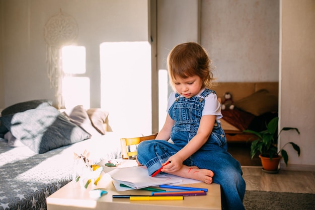Małe dziecko w domu przy dziecięcym stole rysuje flamastrami