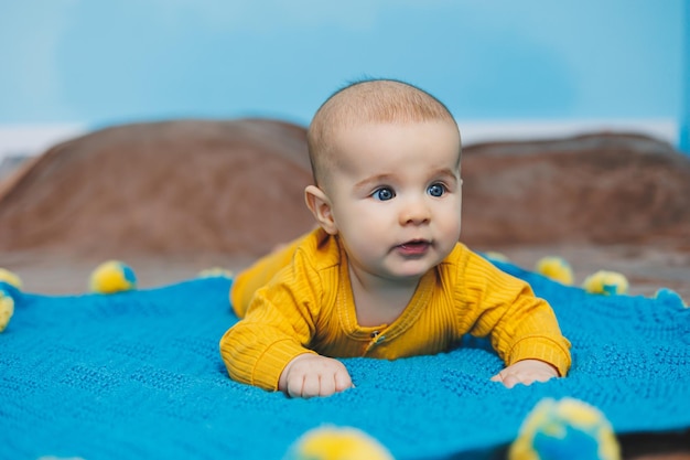 Małe dziecko w wieku 45 miesięcy leży na łóżku w żółtym ubraniu Dziecko zaczyna trzymać głowę Ubranka dla niemowląt