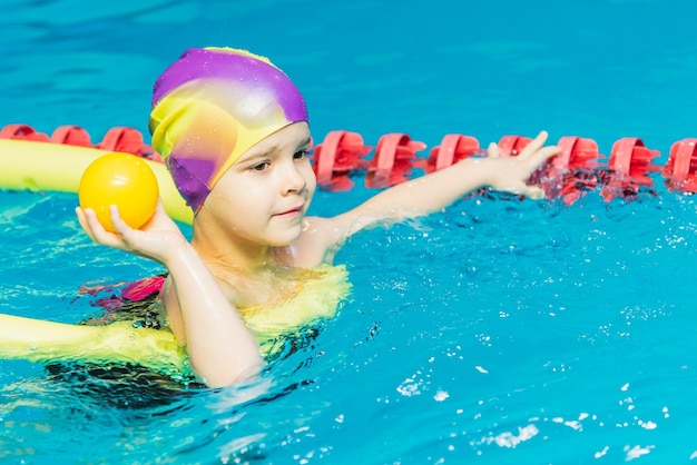 Małe dziecko z kamizelką ratunkową na piersi uczy się pływać w krytym basenie.