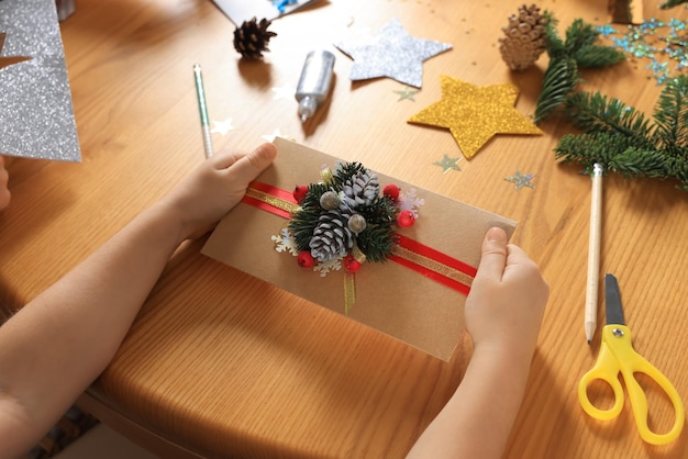 Małe dziecko z piękną kartką z życzeniami świątecznymi na drewnianym stołowym zbliżeniu