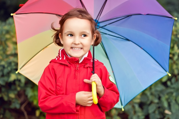 Małe dziecko z wielobarwnym tęczowym parasolem na zewnątrz.