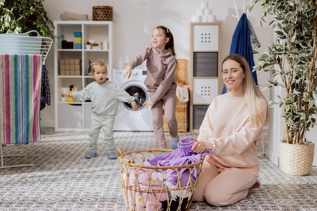 Małe dziewczynki bawią się w łazience, tańcząc w pralni, tańcząc, podczas gdy mama jest zajęta wykonywaniem prac domowych