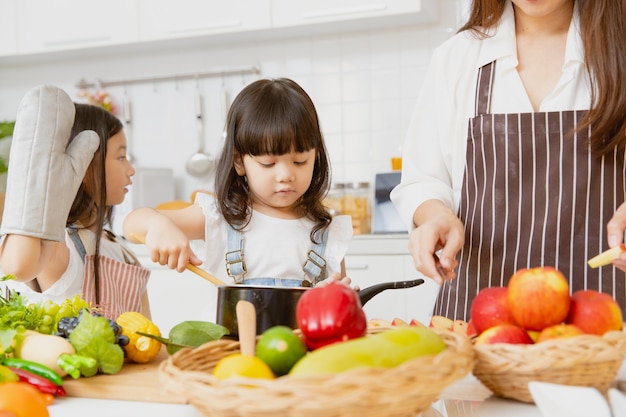 Małe dziewczynki lubią bawić się w gotowanie z mamą i starszą siostrą razem w domu w kuchni na wakacjach