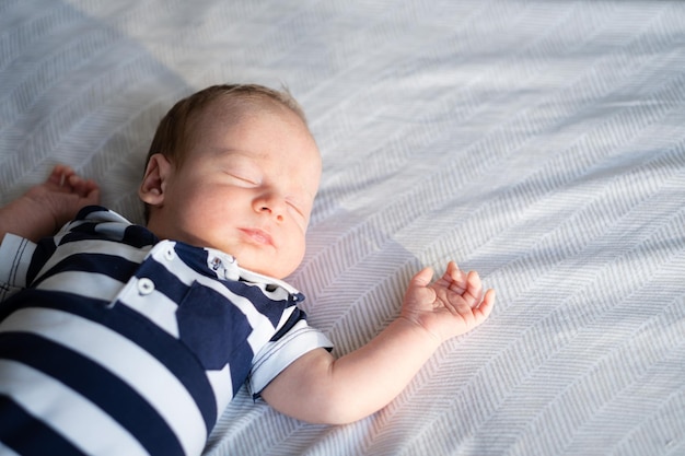 Małe nowo narodzone białe bruneto leżące na plecach na łóżku w prążkowanej koszulce śpiące połowę ciała
