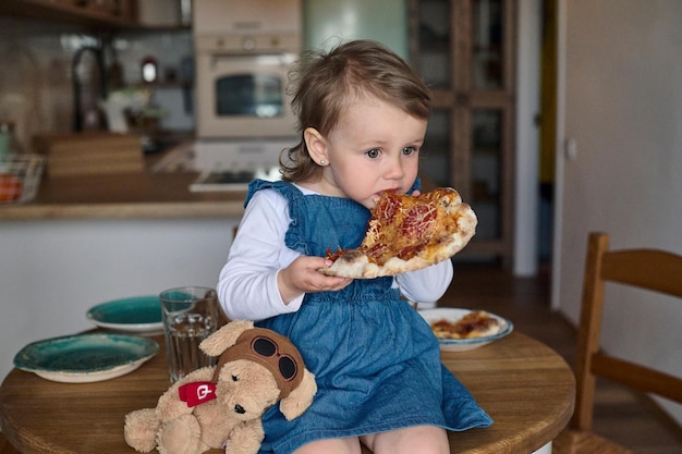 Małe piękne dziecko je pizzę siedząc na stole w kuchni Szczęśliwa koncepcja rodziny