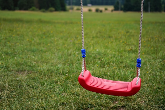 Małe plastikowe dziecko wiszące huśtawka, zamazana łąka w tle