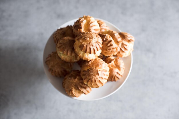 Małe profiteroles na talerzu ze śmietaną na kuchennym stole zbliżenie Gotowanie w domu Widok z góry
