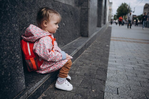 Małe śliczne dziecko, które zgubiło się w mieście dziewczyna w różowym płaszczu przeciwdeszczowym z plecakiem