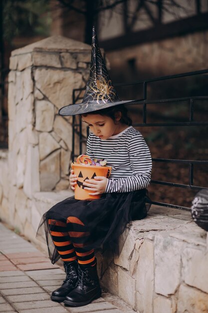 Małe słodkie dziewczyny w stroju wiedźmy trzymając wiadro z dyni jackolantern z cukierkami i słodyczami Kid trick lub leczenia w wakacje Halloween
