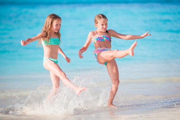 Małe szczęśliwe dzieci świetnie się bawią na tropikalnej plaży, grając razem na płytkiej wodzie.