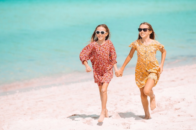 Małe szczęśliwe śmieszne dziewczyny bawią się razem na tropikalnej plaży.