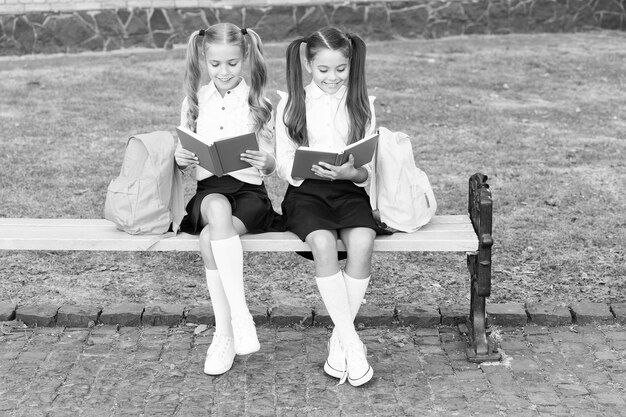 Małe szkolne przyjaciółki z plecakami do czytania książek koncepcji
