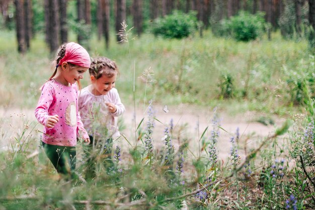 Zdjęcie małe uśmiechnięte dziewczynki w różowych koszulach patrzące na białego motyla na zielonej łące