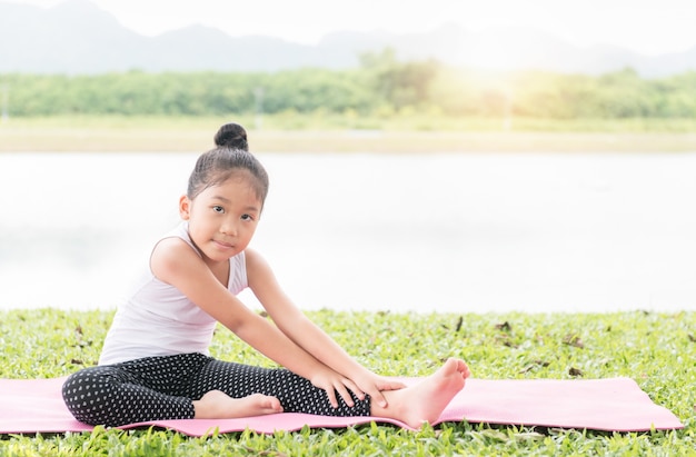 Małej ślicznej azjatykciej dziewczyny joga ćwiczy poza na macie w parku, Zdrowego i ćwiczenia pojęciu ,.