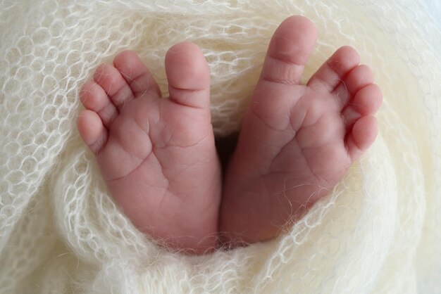 Maleńka stopa noworodka Miękkie stopy noworodka w białym wełnianym kocu Zbliżenie na palce, pięty i stopy noworodka Dziane białe serce w nogach dziecka Fotografia makro