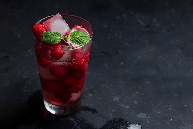 Malinowy koktajl alkoholowy z likierem, lodem i miętą na ciemnym tle. Raspberry Mojito. Orzeźwiający zimny napój, lemoniada lub mrożona herbata w szklance. Zamknij się, skopiuj miejsce na tekst, niski klucz