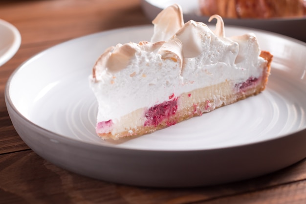 Zdjęcie malinowy tort z białą uwielbianą bezą na drewnianym stole