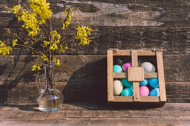 Malowane jajka w pudełku na stole z wazonem z kwiatami. Na tle starych desek. Koncepcja na temat Wielkanocy.