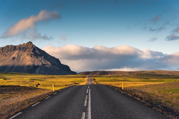 Malownicza pusta asfaltowa prosta droga ze światłem słonecznym i widokiem na góry na Islandii