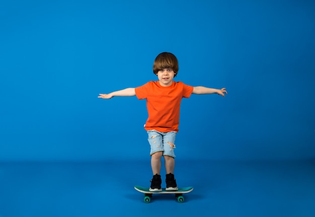 Maluch chłopiec w koszulce i szortach jeździ na deskorolce po niebieskiej powierzchni z miejscem na tekst