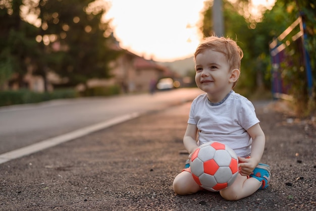 Maluch chłopiec z piłką futbolową na ulicy