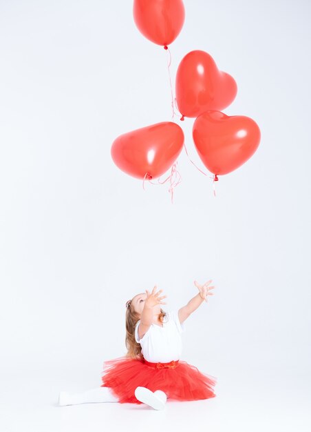 Maluch dziewczyna w czerwonej spódnicy i trzymając balon serce na białym tle. Koncepcja Walentynki.