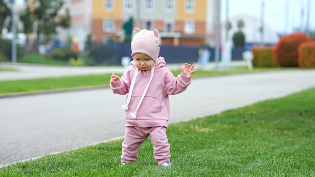 Maluch dziewczynka w różowych ubraniach lubi chodzić po zielonej trawie