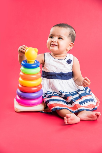 Maluch indyjski lub azjatycki, niemowlę lub dziecko bawiące się zabawkami lub klockami, leżąc lub siedząc na białym tle na jasnym lub kolorowym tle