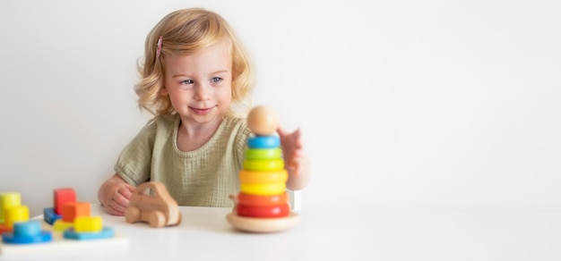 Maluch kaukaski, dziecko, dziewczynka 2 lata, bawi się kolorową drewnianą piramidionem eko. Copyspace.